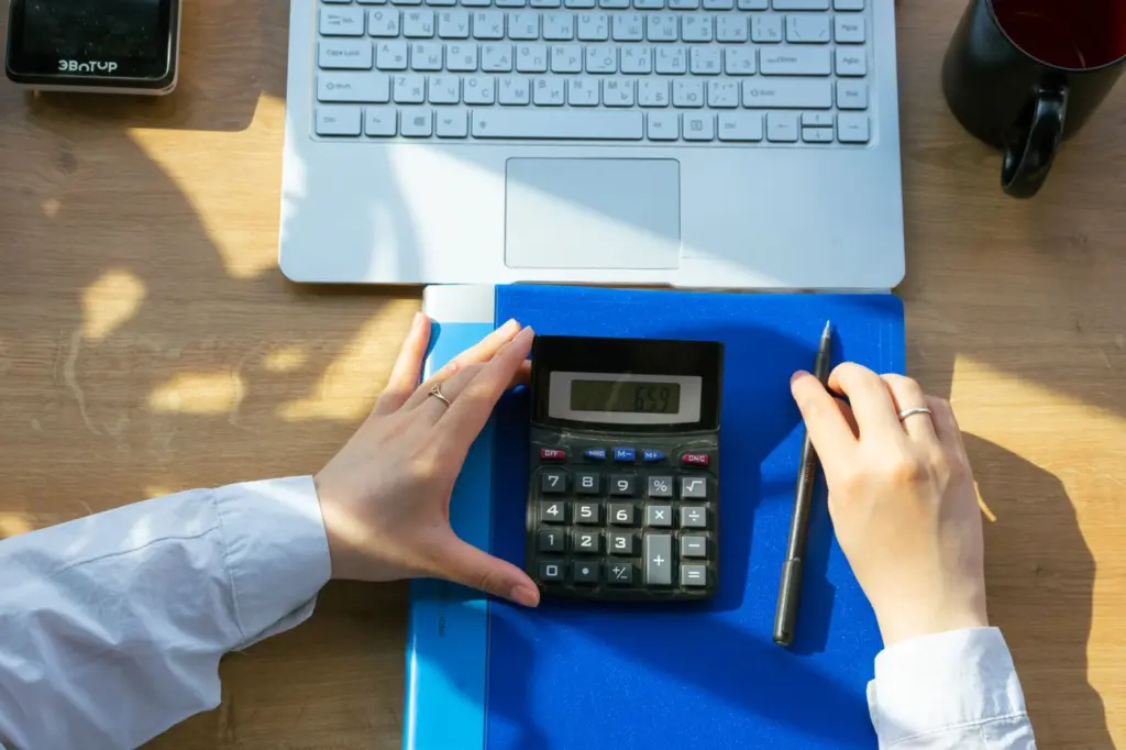 B2B-Preise richtig beurteilen: Einkaufspreis ist nicht alles 1 Hände mit Taschenrechner, Laptop und Notizbuch bei einer Geschäftskalkulation