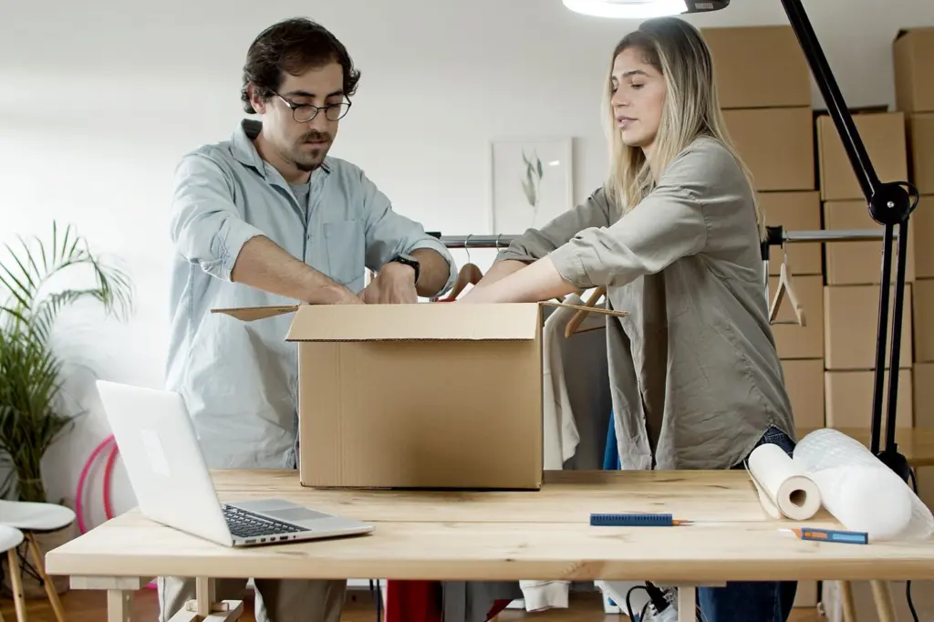 20 Fragen, die du jedem Dropshipping-Lieferanten stellen solltest 1 Zwei Personen verpacken Bestellungen an einem Arbeitstisch mit Laptop und Kartons